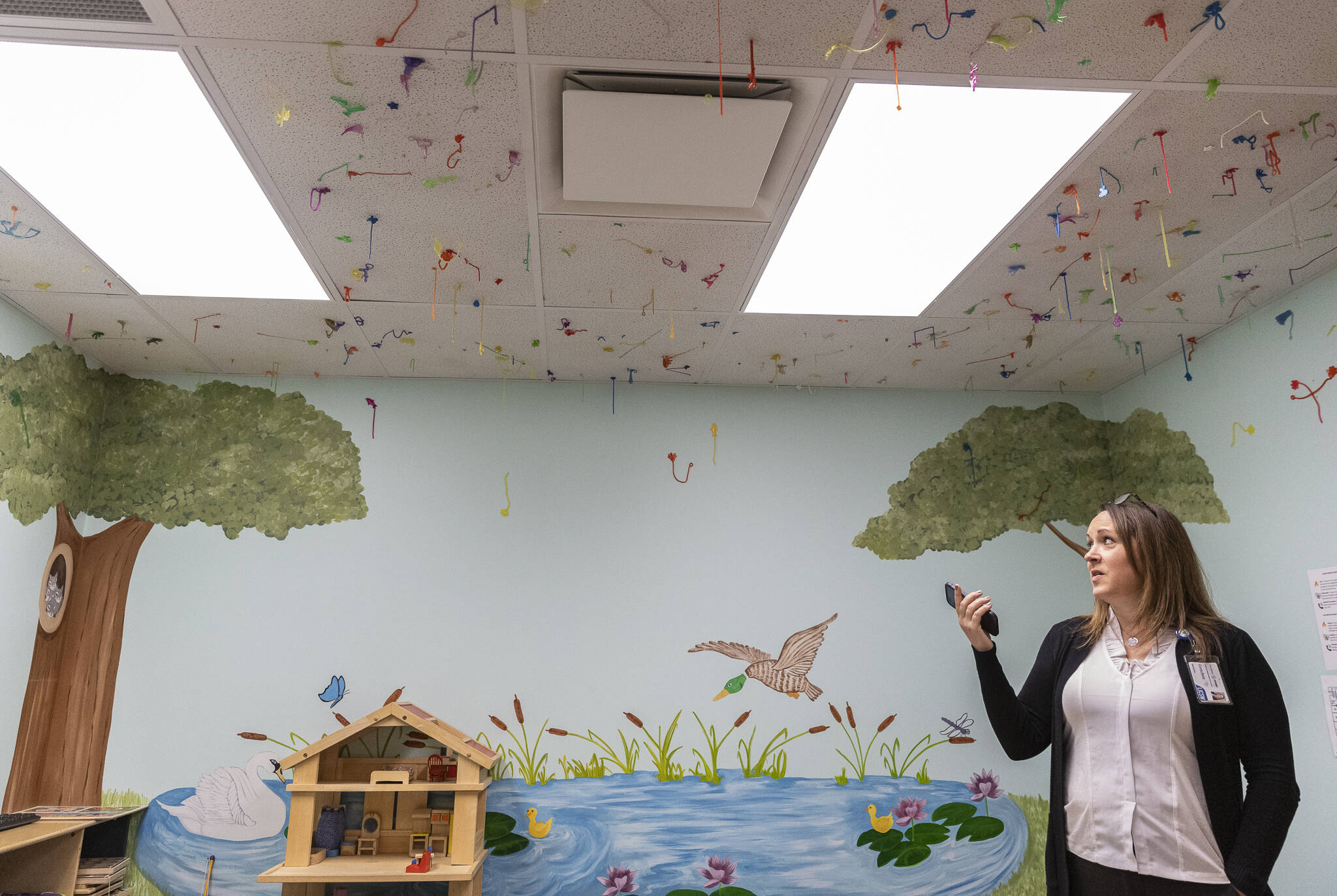 Gretchen Clark Bower explains that each sticky hand hanging from the ceiling was stuck there by a child that came through the exam room at the Providence Intervention Center on Nov. 21, 2025 in Everett, Washington. (Olivia Vanni / The Herald)