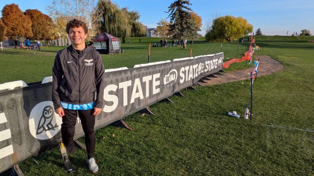Arlington junior Ramon Little stands in front of a state championship banner along the WIAA Cross Country State Championships course at Sun Willows Golf Course in Pasco on Nov. 8, 2025. (Photo courtesy Richard Little)
