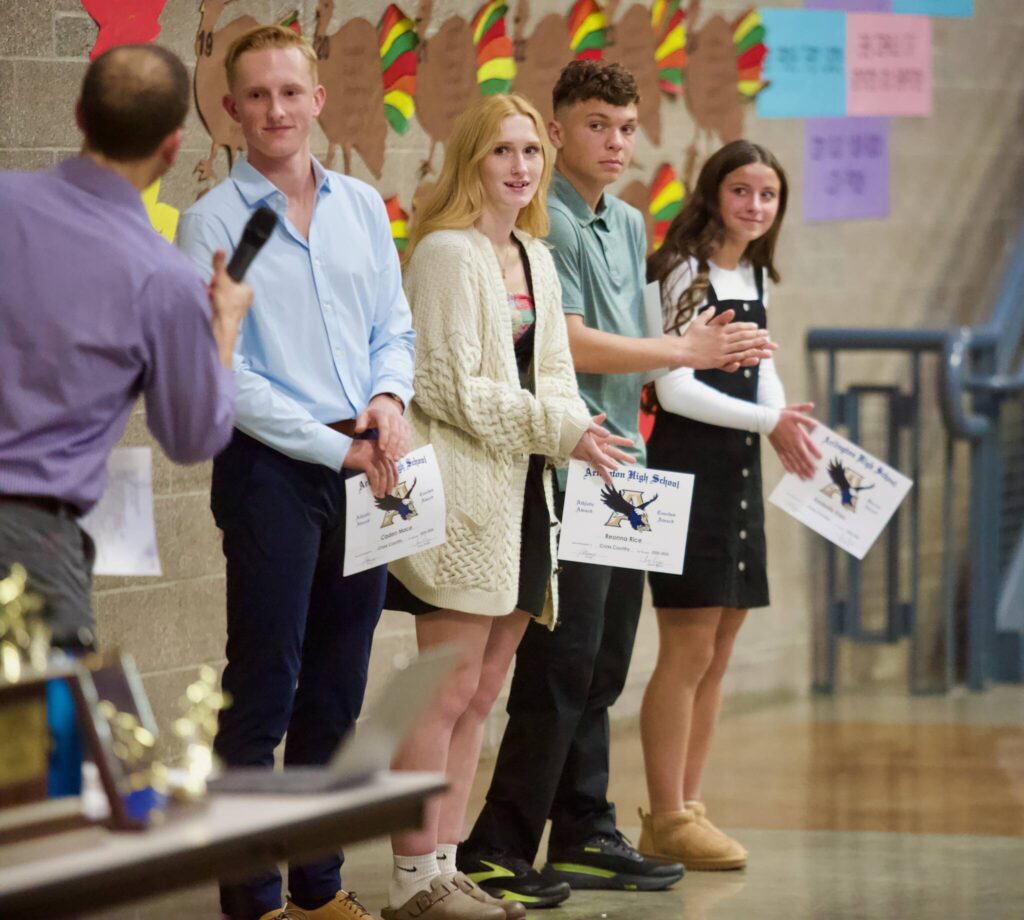 Arlington junior Ramon Little (second from right, in green) stands between fellow team award-winners (from left to right) senior Caden Mace, senior Reaonna Rice and junior Anabelle Klein at the Arlington cross country banquet in the Arlington High School Commons on Nov. 18, 2025. (Joe Pohoryles / The Herald)
