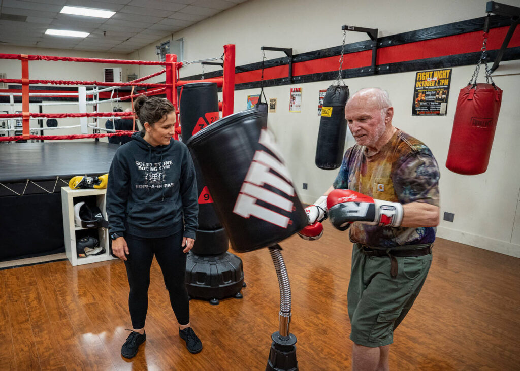 Wil Kerns warms up by punching the bag while Lauren Stone looks on.
