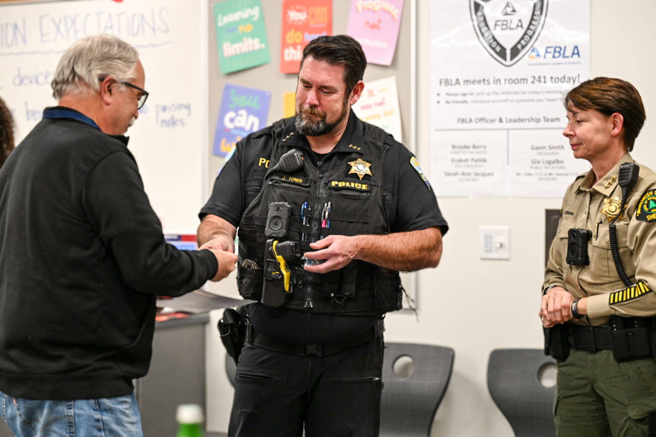 Stanwood Police Chief Jason Toner hands a challenge coin to a graduating member of the police departments first Community Academy on Nov. 18 as Snohomish County Sheriff Susanna Johnson looks on. (Provided photo)