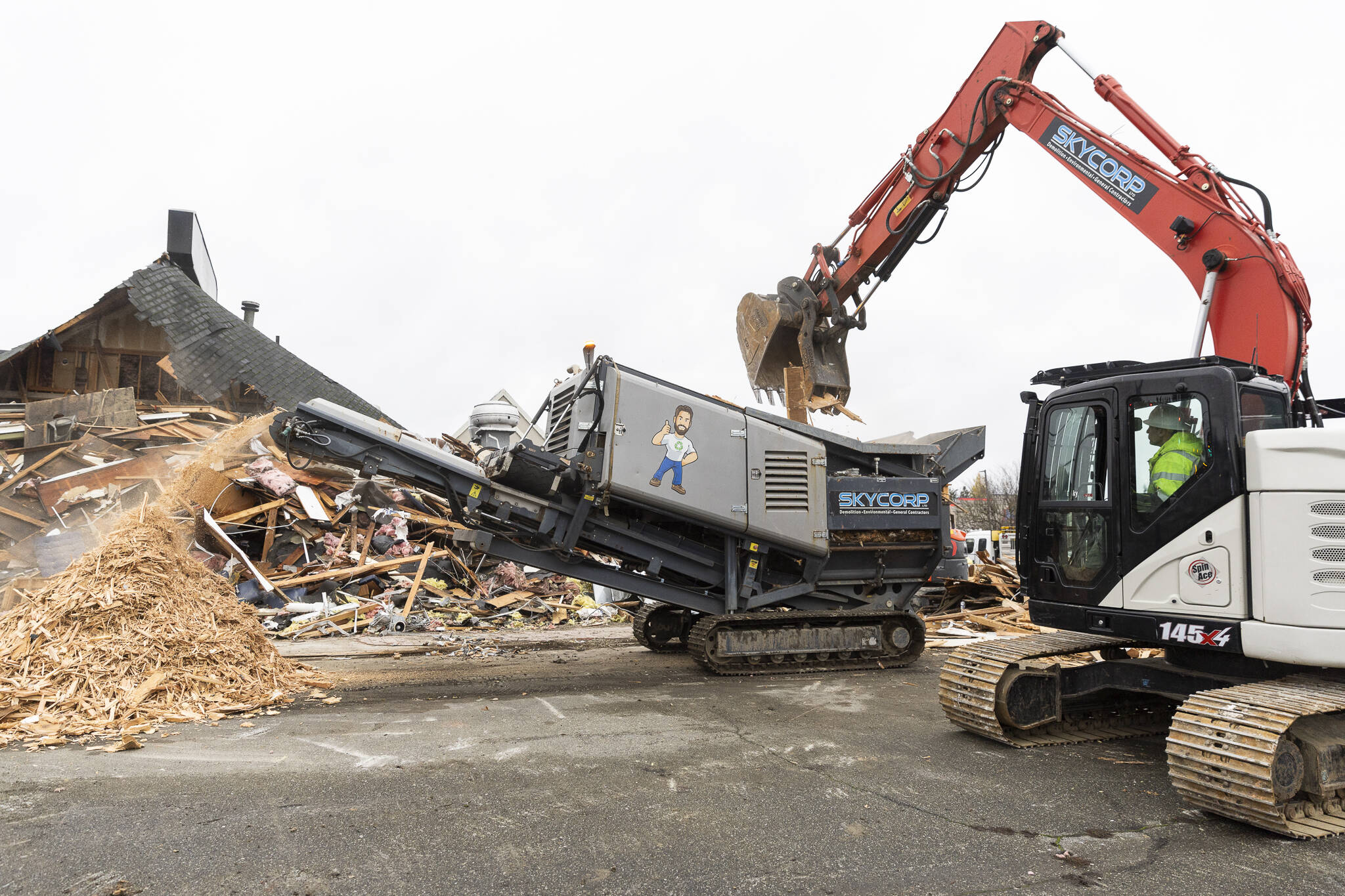 An excavator moves wood into a machine to be stripped of metals and recycled during demolition at the site of a new Sno-Isle library along 128th Street on Nov. 25, 2025 in Everett, Washington. (Olivia Vanni / The Herald)