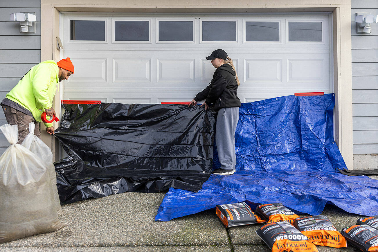 Bella Reid, right, and her fiancé Hector Rodrigues cover their garage door with tarps and water activated flood bags in preparation for potential flooding on Tuesday, Dec. 9, 2025 in Snohomish, Washington. (Olivia Vanni / The Herald)