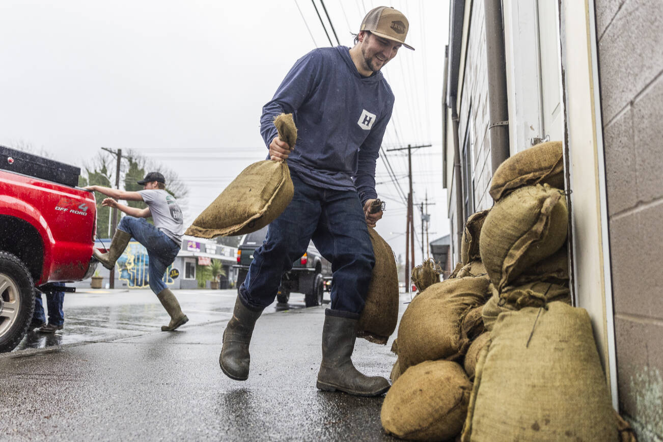 Zach Day sandbags the entrance to his grandparents residence along Main Street on Wednesday, Dec. 10, 2025 in Sultan, Washington. (Olivia Vanni / The Herald)