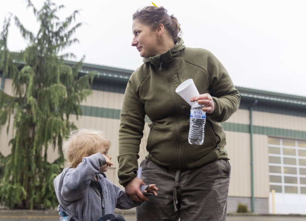 Ashlie Coffin holds the hand of her son Junior, 2, outside of the Evergreen State Fairgrounds Red Cross disaster relief shelter where her and her two sons have been staying for the last two days after their trailer at Three Rivers Mobile Home Park flooded on Friday, Dec. 12, 2025 in Monroe, Washington. (Olivia Vanni / The Herald)

