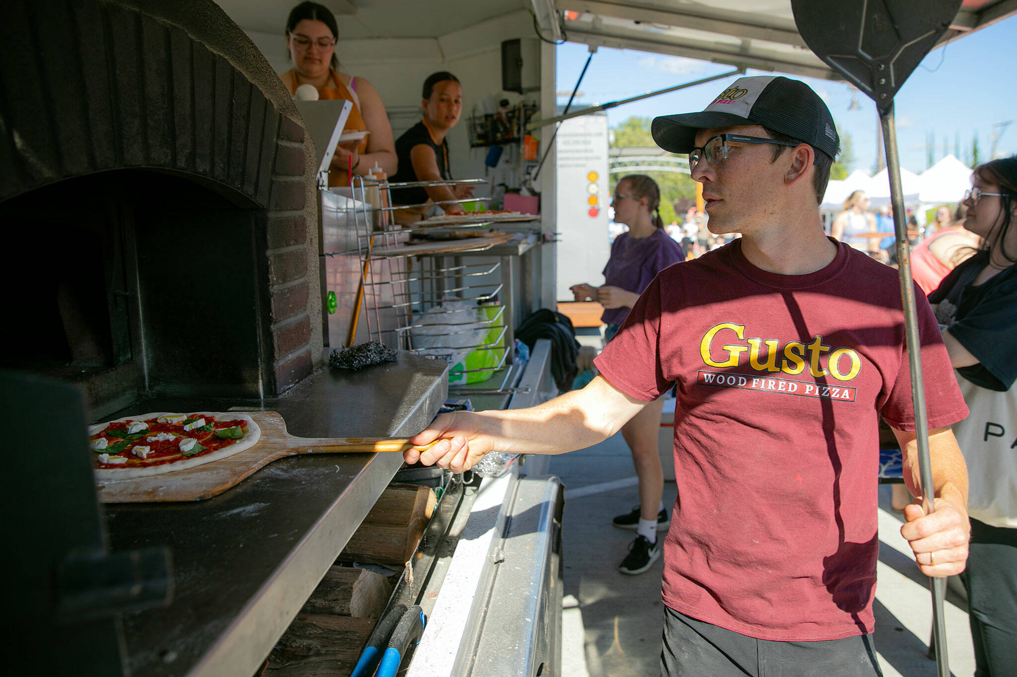 Zach Meyer, who owns Gusto Wood Fired Pizza with his wife Lindsay, throws a Margherita pizza into the oven while cooking at the Lake Stevens Farmers Market on Wednesday, June 12, 2024, in Lake Stevens, Washington. (Ryan Berry / The Herald)