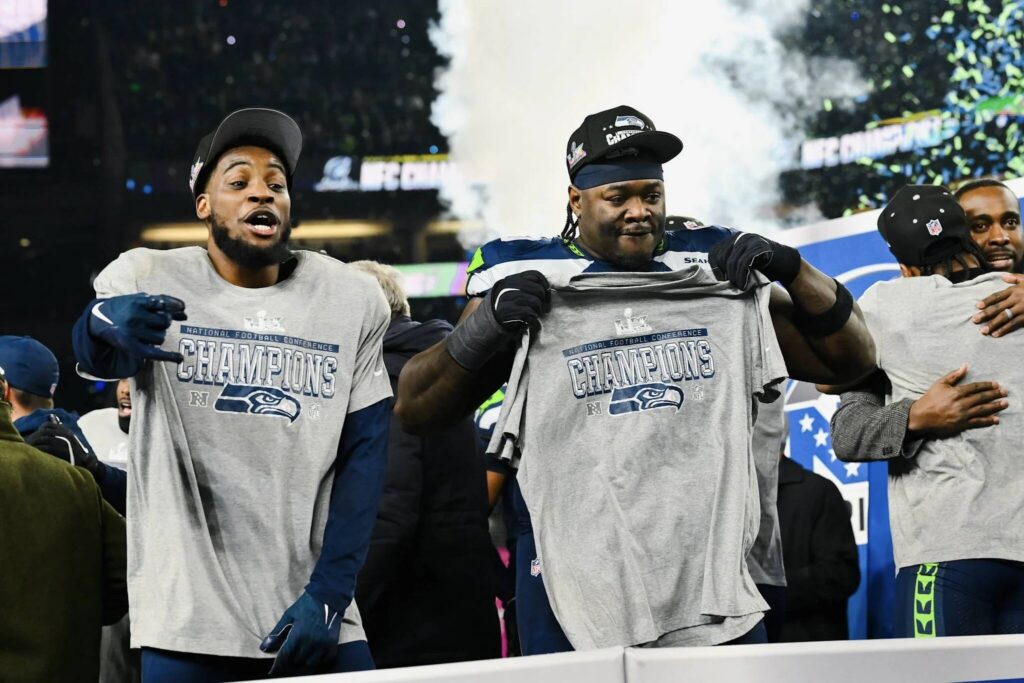 Seahawks defensive tackle Jarran Reed (right) and cornerback Devon Witherspoon hold up NFC Championship T-shirts at Lumen Field in Seattle, Washington on Sunday, Jan. 25, 2026. (Photo courtesy of the Seattle Seahawks)
