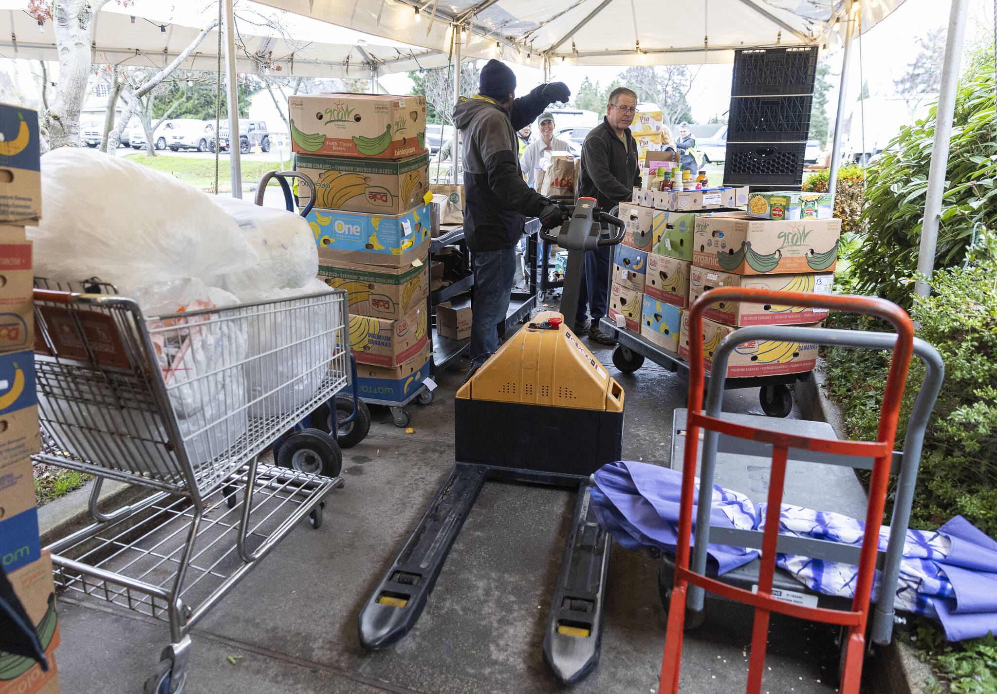Volunteers and employees navigate through a tented and crowded walkway as donations come in and food is brought out to waiting customers at the Edmonds Food Bank on Monday, Dec. 8, 2025 in Edmonds, Washington. (Olivia Vanni / The Herald)