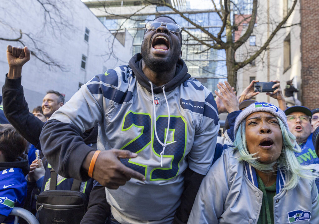 Malik Weary, left, and Cherise Hester, right, cheer as players pass by along 4th Avenue during the Seahawks World Champions Parade on Wednesday, Feb. 11, 2026, in Seattle, Washington. (Olivia Vanni / The Herald)
