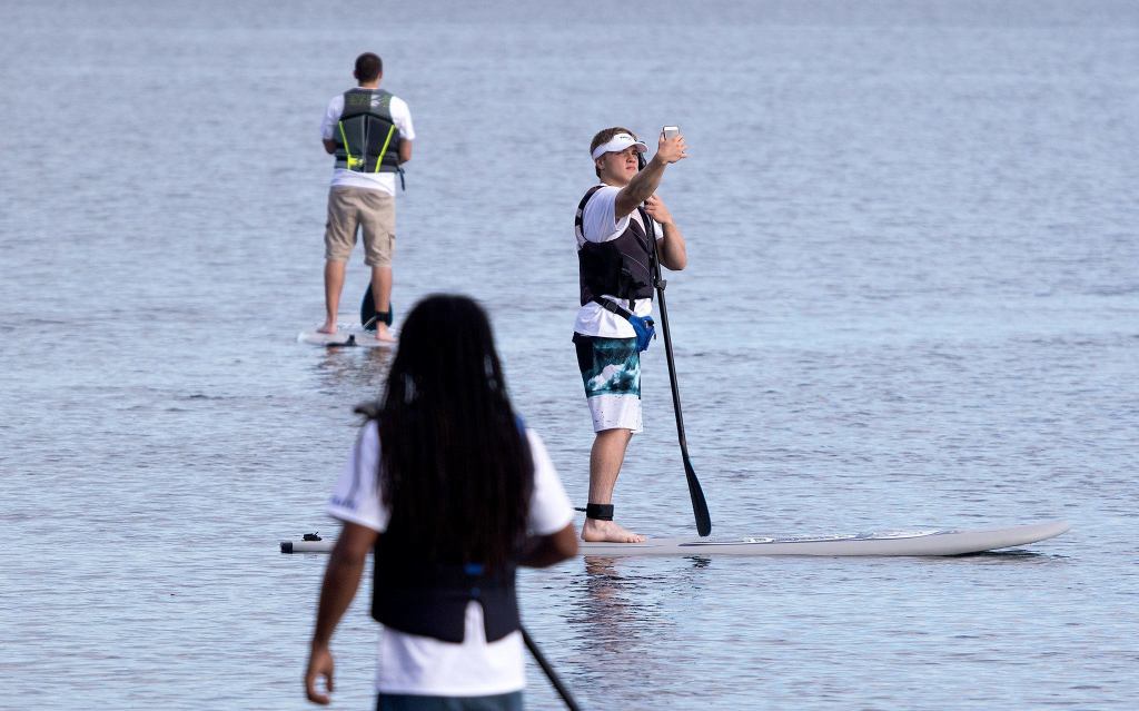 Surrounded by water, Paddle Broz employee Jaxson Sweum risks a selfie photo as he and others practice stand-up paddleboarding at Lundeen Park on Monday in Lake Stevens. (Andy Bronson / The Herald)