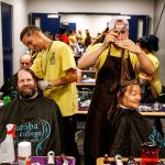 At the first work stations in a long line, Paroba College of Cosmetology volunteer Alex Frazier (left) cuts the hair of Cody Phillips while David Hutton, another cosmetology volunteer, does Lohti Hevly&rsquo;s hair during Project Homeless Connect, which was held at Everet High School on Thursday. (Dan Bates/The Herald)