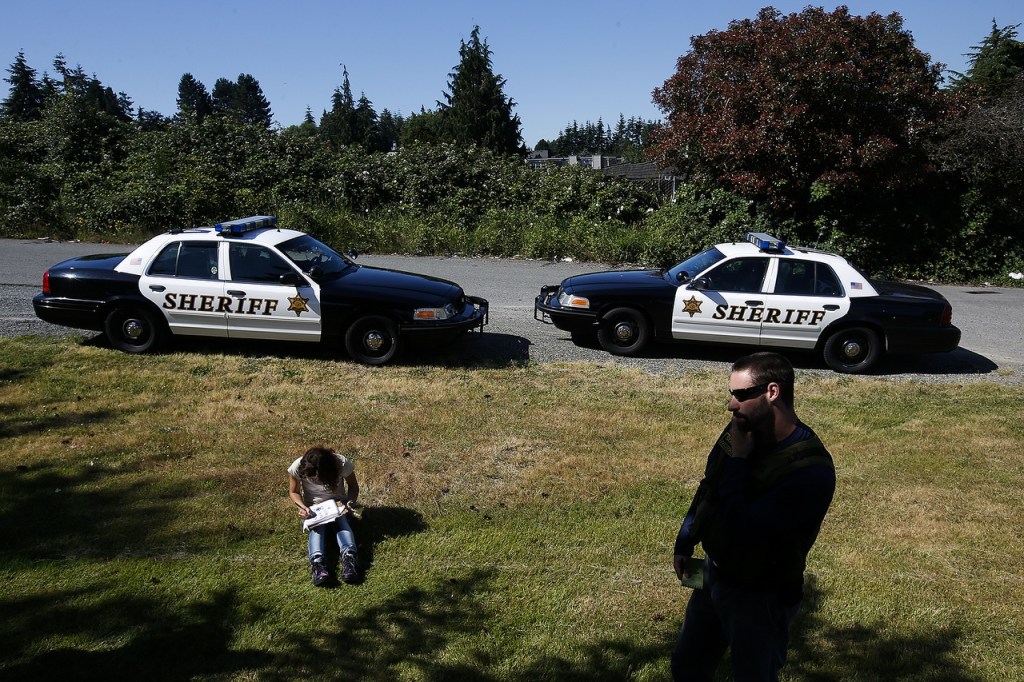 A young heroin addict waits in the grass near 128th Street Southwest as Snohomish County social worker Jesse Calliham (right) stays on the line waiting for confirmation that she would have a hotel room to stay in on June 29. After being on hold for 27 minutes, Calliham was finally able to secure a room for her which allowed for an easier transition into treatment. (Ian Terry / The Herald)
