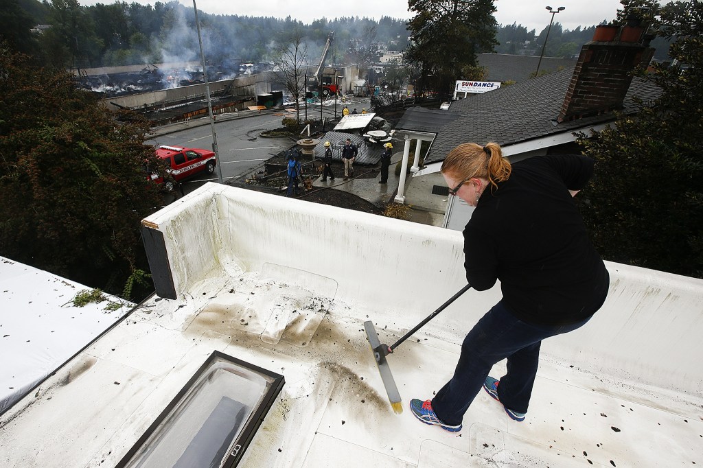 Jennifer Herrman sweeps soot and debris from the roof of Zulu&rsquo;s Board Game Cafe at the corner of Main Street and 103rd Avenue Northeast in downtown Bothell on Friday. &ldquo;I&rsquo;m amazed, it&rsquo;s not as bad as it could have been,&rdquo; Herrman said of damage to the cafe. Herrman&rsquo;s brother saw flames on a security camera early Friday morning and rushed to the cafe immediately. (Ian Terry / The Herald)