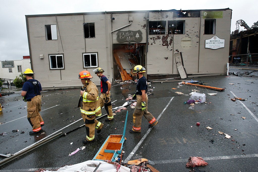 Firefighers pass by the entrance to the Bothell Mall following a fire on Friday. (Ian Terry / The Herald)