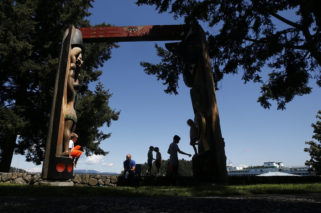 Children playing are silhouetted beneath native artist Susan Point&rsquo;s red cedar house post sculpture in Friday Harbor. (Ian Terry / The Herald)