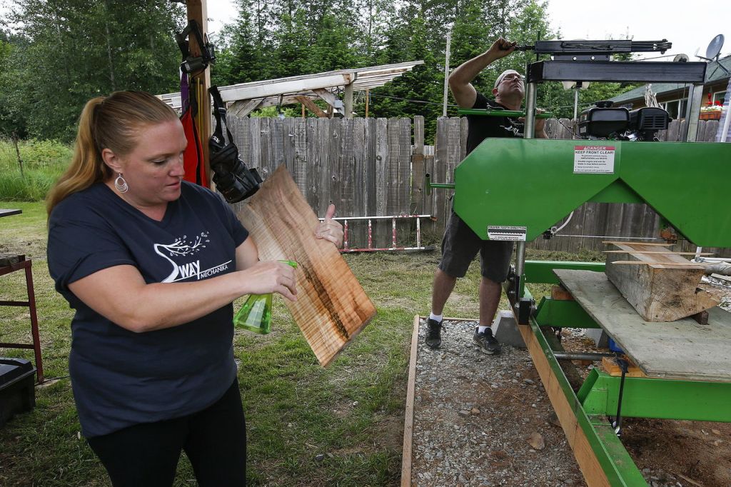 Teresa Hanna sprays water on a cut of wood to reveal its grain while Mark prepares their saw mill to cut through a piece of salvaged wood.