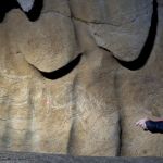 An archaeologist points to a another drawing in the cave.
