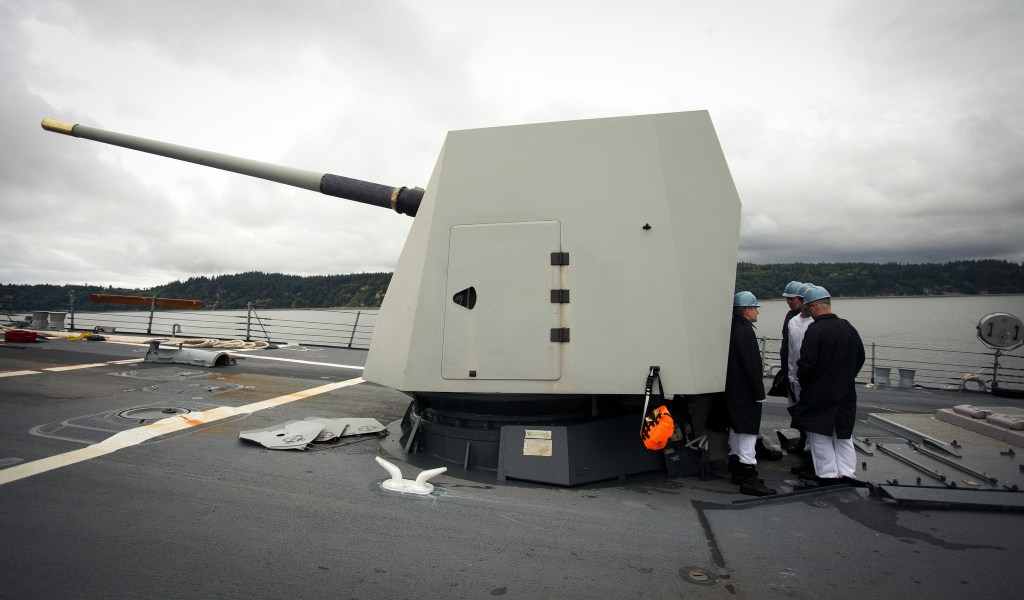 Sailors use a 5-inch gun turret to hide from a cold wind as the USS Gridley leaves Everett on a trip to Seattle for Seafair on Tuesday. (Andy Bronson / The Herald)