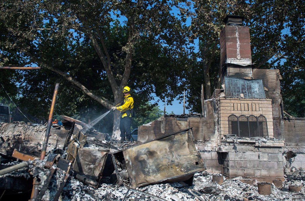 Dan Peters, with the Nevato Fire District, mops up a fire at a house during the Clayton fire after structures were destroyed in Lower Lake, California, on Monday. (Hector Amezcua/The Sacramento Bee via AP)