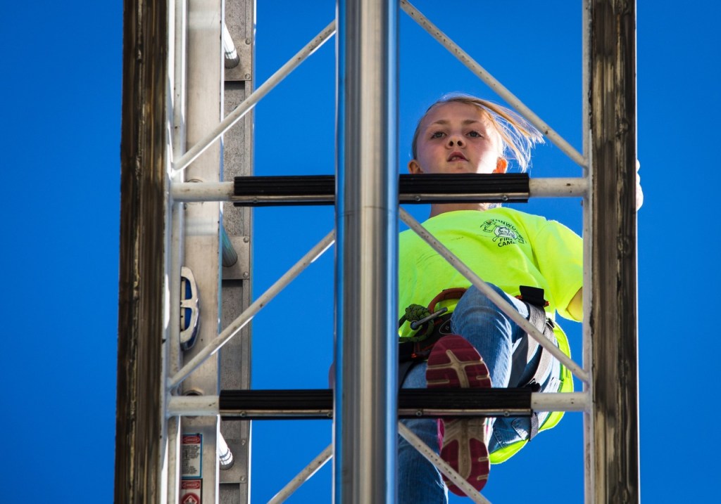 Rikki Miller, 9, makes her way up the 100-foot aerial ladder during the Lynnwood Kids Fire Camp on Thursday. Members of the Lynnwood Fire Department organize group activities for the kids that promote teamwork, including a ladder walk, extinguishing fires and saving a life with ropes. (Daniella Beccaria / For The Herald)