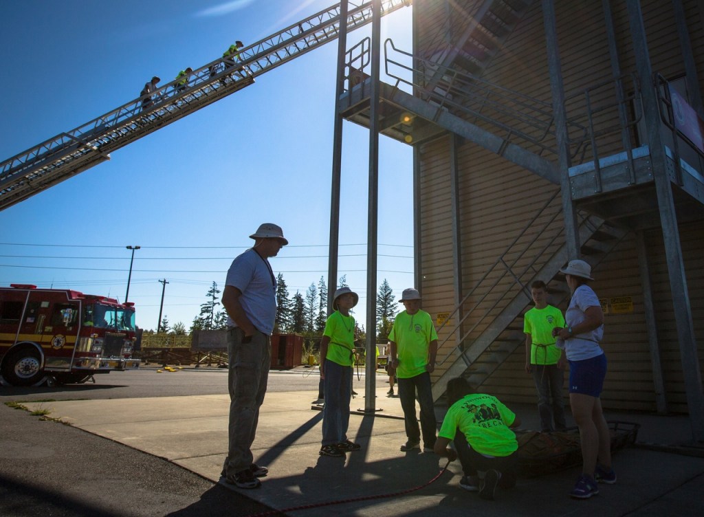 A group of campers learn how to fasten a rope while three others climb their way up the 100-foot aerial ladder during the Lynnwood Kids Fire Camp on Thursday. Members of the Lynnwood Fire Department organize group activities for the kids that promote teamwork, including a ladder walk, extinguishing fires and saving a life with ropes. (Daniella Beccaria / For The Herald)