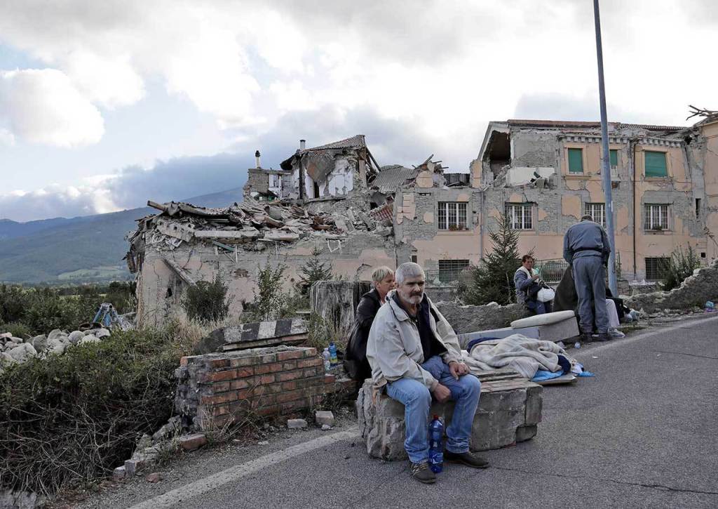 People sit on the side of a road as collapsed buildings are seen in the background following an earthquake, in Amatrice, Italy, on Wednesday. (AP Photo/Alessandra Tarantino)