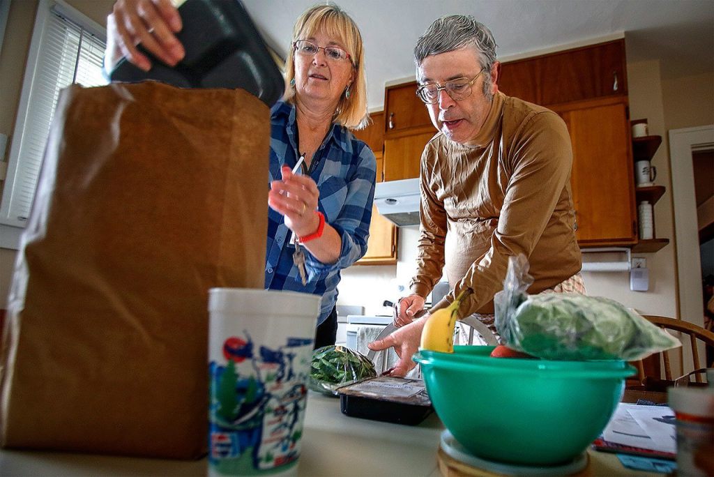 Meals on Wheels driver Jane Slager helps Cliff Porter, 69, of Everett, go through a bagful of groceries at his kitchen table. (Dan Bates/The Herald)
