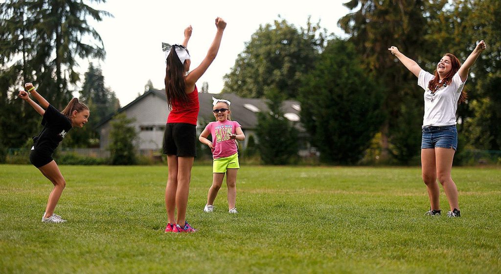 Cassie Kunselman, 15, (left) leades 7-year-old Jaelyn Fox (pink) Alawna Schweitzberger, 11 (red) and Amaya Villalobos, 7 (left) stretching and warming up to do a cheerleading practice session on the athletic field at Jennings Park in Marysville. (Dan Bates / The Herald)