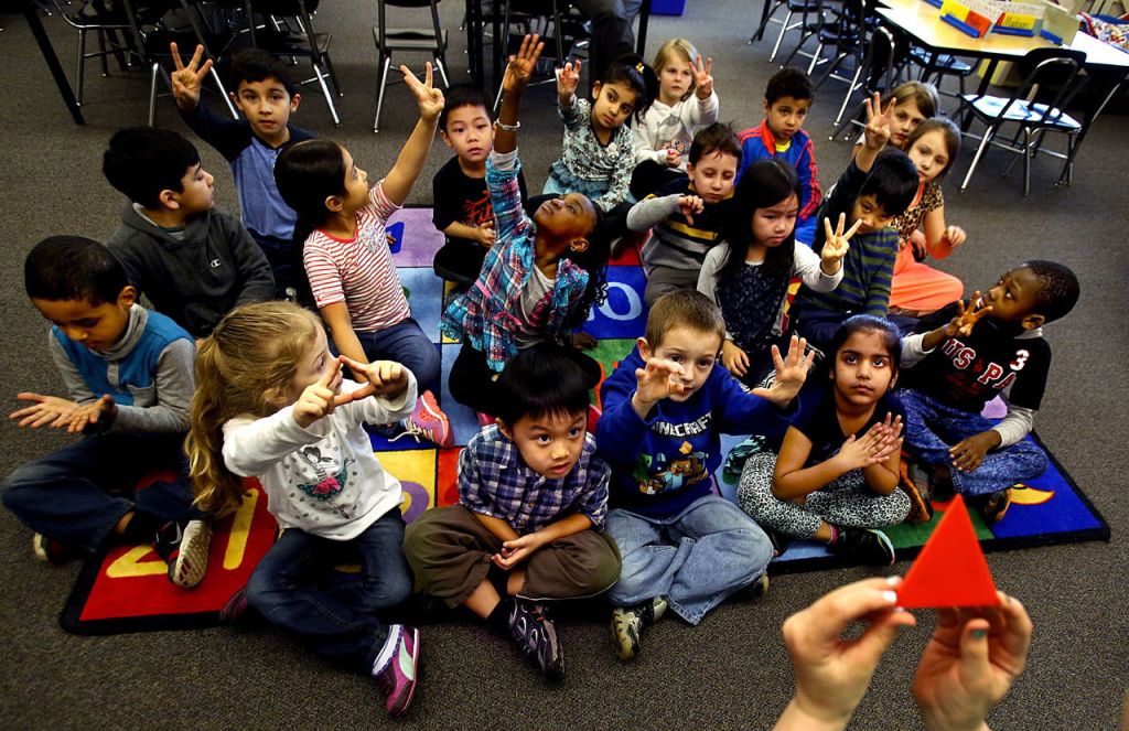 Along with other geometric shapes, student Daphne McDowell holds up an orange triangle (lower right) while her kindergarten classmates answer questions from teacher Judi Rouse about its characteristics.