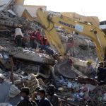 Rescue workers recover a body from the rubble Tuesday, as a bulldozer removes the debris of a collapsed building felled by the earthquake.