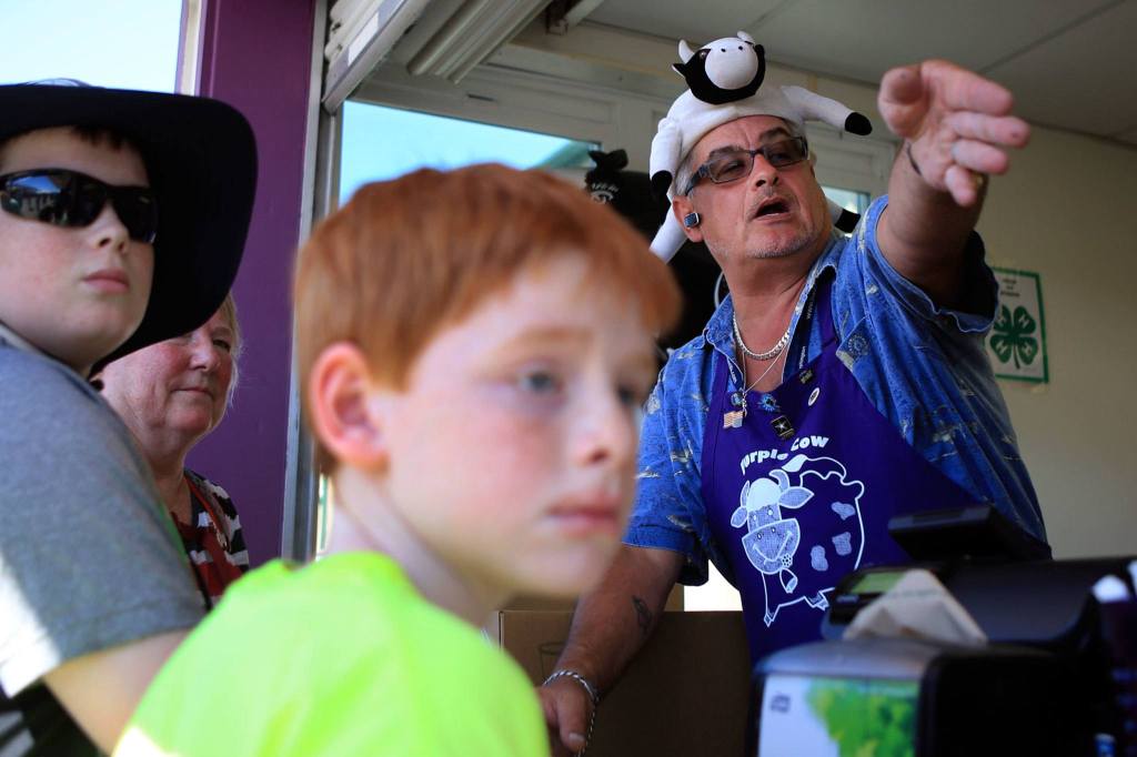 Rod Courtney, right, directs fair goers where to pick up their Purple Cow floats during the first day of the Monroe fair. (Kevin Clark / The Herald)