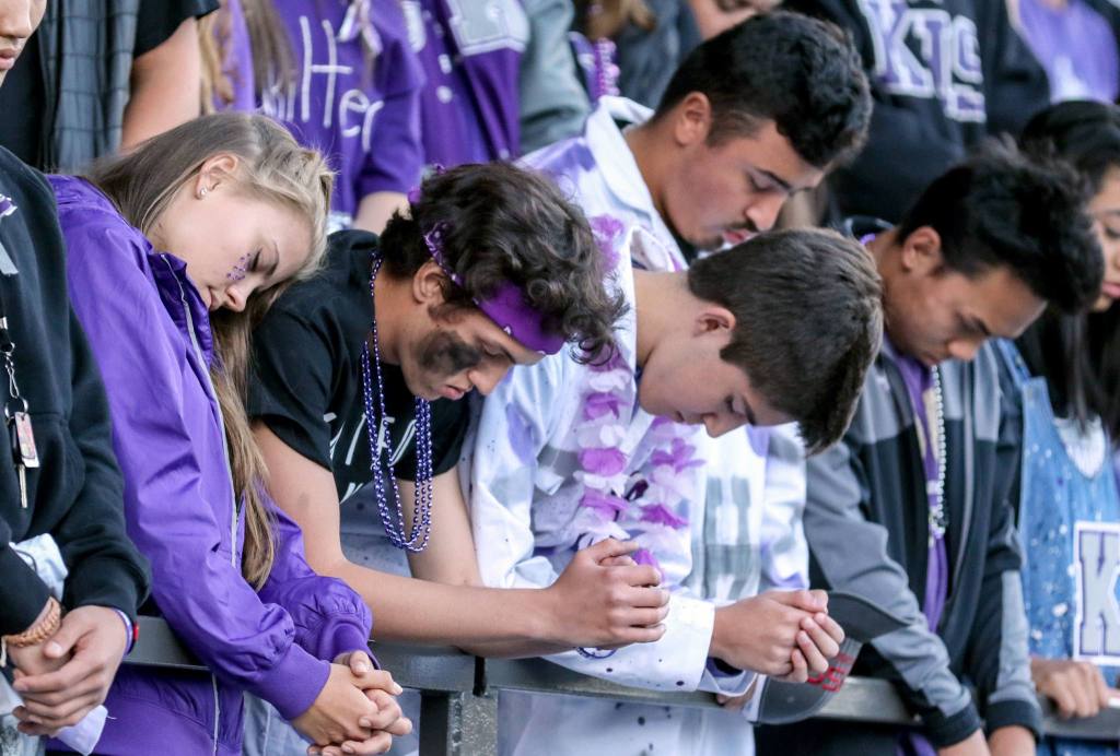 Fans bow their heads for a moment of silence for the victims of the Mukilteo shooting during a memorial service before the start of Kamiak&rsquo;s game against Bishop Blanchet Friday night at Goddard Stadium in Everett. (Kevin Clark / The Herald)