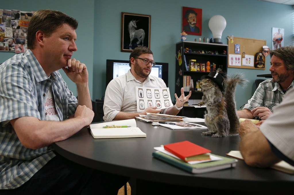 Scott Heffernan, center, discusses design concepts as David Wahl, left, and Curt Hanks listen during a daily meeting at the Archie McPhee warehouse in Mukilteo. (Ian Terry / The Herald)