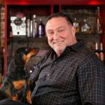 Brenton Holland, sits with his dog, Sophie, at the bar of his recently acquired Prohibition Grille & Saloon restaurant. (Dan Bates / The Herald)