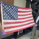 Everett Mayor Ray Stephanson (right) and Deputy Police Chief Mark St. Clair help display a flag that is believed to be linked to a famous photo of ground zero in New York after the Sept. 11, 2001, terrorist attacks. The flag turned up in Everett in 2014 when an unidentified man dropped it off at a fire station. (City of Everett)