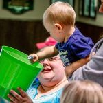 Treasurer Nikki Jones holds the bucket of entries while William Postma, held by his mother, Jessica Postma, draws the winning ticket for a pre-game field pass at an upcoming Seahawks game. The 18-month-old William drew his own great-grandmother&rsquo;s name, Barbara Callaghan. (Dan Bates / The Herald)