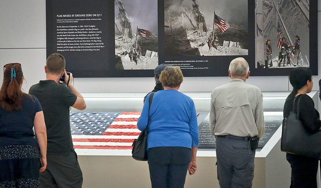 Visitors view the display for the American flag, left, that firefighters hoisted at ground zero in the hours after the 9/11 terror attacks, Thursday at the Sept. 11 museum in New York. After disappearing for more than a decade the 3-foot-by 5-foot flag was donated to the museum after it was turned in two years ago by an as-yet-unidentified man at a firehouse in Everett, Washington. (AP Photo/Bebeto Matthews)