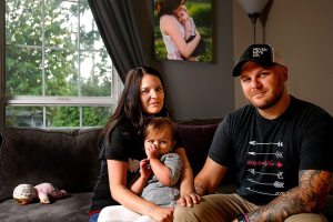 Stephanie and Jeff Reid spend time at home in Marysville with their 2-year-old daughter, Kenley. In a photograph on the wall behind them, Stephanie holds their baby daughter, Blake, who died Aug. 10 of spinal muscular atrophy, or SMA. (Dan Bates / The Herald)