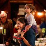 Oh, what a night! Cathy Merchant, of Redmond, carries her 2-year-old daughter, Inara, on her shoulders as she negotiates a big crowd while attending a fundraiser for the Interfaith Association&rsquo;s family shelter, at Forest Park&rsquo;s Floral Hall on Wednesday. (Dan Bates / The Herald)