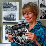 In her home in Everett, artist Deb Fox holds a copy of a new graphic novel she created based on the Everett Massacre. Photocopies of historic photographs hang on her studio wall behind her. She created the art for the graphic novel using charcoal. (Dan Bates / The Herald)