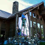 Executive director and assistant sign hanger, Wyonne Perrault, slips around the bottom of the ladder to help her husband, Joe, install a large banner Wednesday outside the new North Counties Family Services facility in Darrington. (Dan Bates / The Herald)