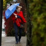 A pedestrian uses an umbrella to shield herself from the wind as she crosses 2nd Avenue North near Main Street in downtown Edmonds on Friday afternoon. (Ian Terry / The Herald)