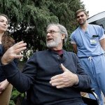 Stephen DeMont, center, sits in a wheelchair at the bus stop where he says that Zach Forcade, right, and Madeline Dahl saved his life days earlier in front of the University of Washington Medical Center on Wednesday, Oct. 19, in Seattle. (AP Photo/Elaine Thompson)