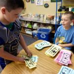 Artemis Batchelor, right, pays out classmate Cooper Rysemus&rsquo; earnings in Froggy Dollars in Lisa Holland&rsquo;s classroom at Mount Pilchuck Elementary School in Lake Stevens on Sept. 30. It was &ldquo;payday&rdquo; at the class bank, part of a yearlong financial education project by Holland that culminates in a student marketplace. (Contributed photo)