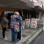 Thoughtful Israel hug 2 Bits and More owner Dawn Ambler on the sidewalk beside the burned out remains of the indoor flea market and thrift shop on Tuesday, Oct. 25, 2016 in Arlington, Wa. At left is Ambler&rsquo;s niece Jeness Crtiz. (Andy Bronson / The Herald)