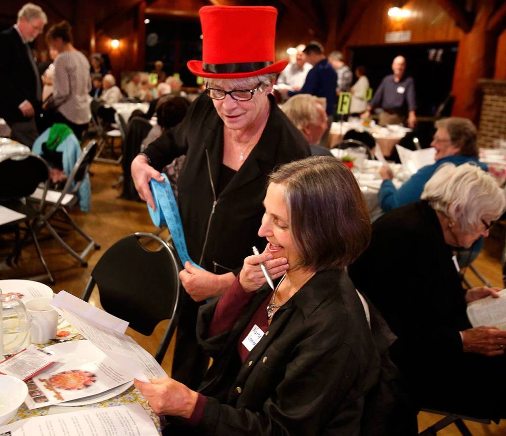 In the bright red top hat, Cyndie Henderson is 10 seconds away from convincing Nancy Lombard of Snohomish to buy some raffle tickets Wednesday night at the Interfaith Fundraiser in Everett. Lombard bought $20 worth of the tickets. (Dan Bates / The Herald)