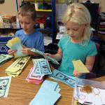 Artemis Batchelor, left, and Andi Elshaug serve as bankers, handing out Froggy Dollars to classmates in Lisa Holland&rsquo;s classroom at Mount Pilchuck Elementary School in Lake Stevens on Sept. 30. It was &ldquo;payday&rdquo; at the class bank, part of a yearlong financial education project by Holland that culminates in a student marketplace. (Contributed photo)