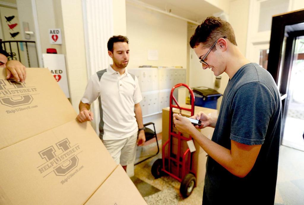 Brett Barry, left, waits for St. Joes student Nick Boehman to check the manifest on his smart phone before the boxes are taken up to his dorm room. (Michael Bryant/Philadelphia Inquirer)