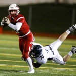 Snohomish quarterback Brandon Jodock (left) looks to pass as he&rsquo;s wrapped up by Arlington defender Logan Cartwright during a district play-in game Tuesday at Snohomish High School. (Ian Terry / The Herald)