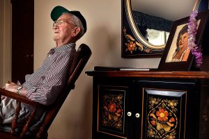 Raymond Lund, 95, a World War II veteran who served in Europe, including landing on the beach at Normandy on D-Day, sits in a rocker at his home in Stanwood. A framed photograph of his wife, Aileen sits on a cabinet behind him with a lei hanging over it. Aileen, who died last year, and Ray were married for 65 years. (Dan Bates / The Herald)